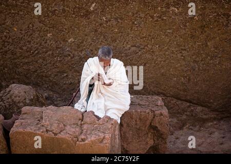 Uomo in bianco che legge la bibbia a Biete Medhane Alem / Biet Medani Alemn, monolito ortodosso sotterraneo squarciato chiesa a Lalibela, Etiopia, Africa Foto Stock