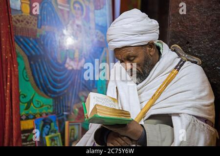 Sacerdote che legge la bibbia a Biete Medhane Alem / Biet Medani Alemn, monolito ortodosso squarciato in pietra a Lalibela, Etiopia, Africa Foto Stock