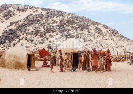 Tribù Himba le popolazioni indigene della Regione Kunene della Namibia settentrionale, Africa sud-occidentale si riuniscono attorno ad una tipica capanna di fango nel complesso del villaggio Foto Stock