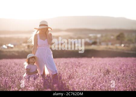 Madre e figlia del bambino 1-2 anni che posa in campo di lavanda indossando abiti e cappelli eleganti all'aperto su sfondo natura. Maternità. Estate ti Foto Stock