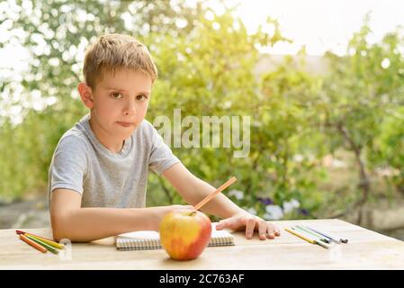 Il ragazzo carino disegna con matite ancora vita. Aria aperta. Giardino sullo sfondo. Concetto creativo. Foto Stock