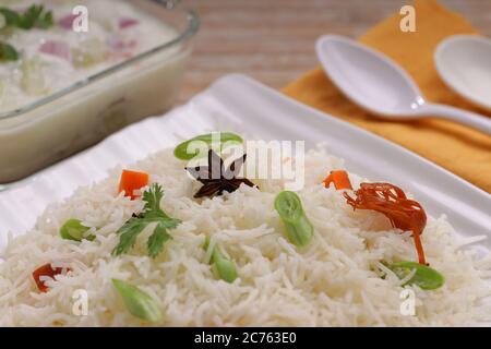 Il Pulav o Pulao, ottenuto con riso basmathi, verdure e spezie indiane.Raita come contorno, è stato sistemato in un piatto bianco quadrato di colore legno Foto Stock