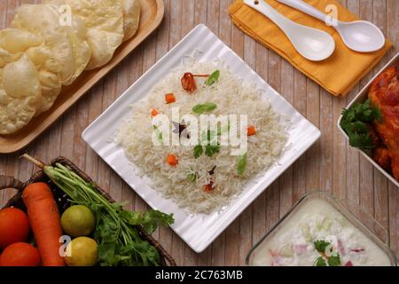 Vista dall'alto di Veg Pulav o Pulao con contorno di pollo fritto, raita e paapad e un cestino pieno di verdure fresche disposte in legno Foto Stock