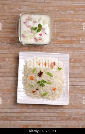 Il Pulav o Pulao, ottenuto con riso basmathi, verdure e spezie indiane.Raita come contorno, è stato sistemato in un piatto bianco quadrato di colore legno Foto Stock