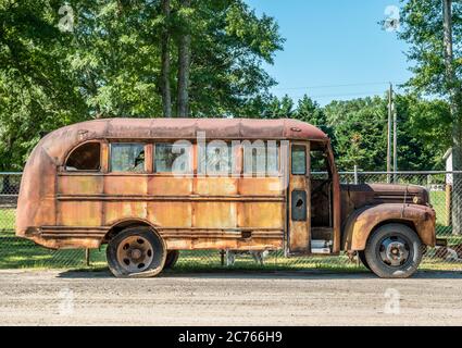 Un vecchio autobus scolastico arrugginito con finestre in vetro rotte e pneumatici piatti si trova trascurato vista laterale all'aperto Foto Stock