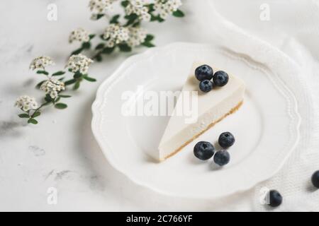 Cheesecake al mirtillo su un piatto bianco, tessuto di pizzo e un ramo con fiori. Foto Stock