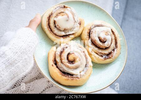 Mano in pullover bianco che tiene piatto di dolci alla cannella fatti in casa Foto Stock