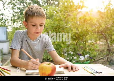 Il ragazzo carino disegna con matite ancora vita. Aria aperta. Giardino sullo sfondo. Concetto creativo. Foto Stock