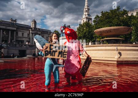 Londra / UK - 07/11/2020: Coppia che indossa costumi e che tiene banner in piedi nella fontana dopo che il gruppo di diritti animali gira fontane rosso in Foto Stock
