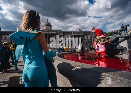 Londra / UK - 07/11/2020: Coppia che indossa costumi e che tiene banner in piedi nella fontana dopo che il gruppo di diritti animali gira fontane rosso in Foto Stock