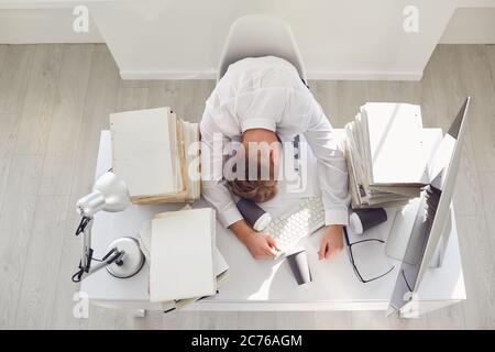 Un uomo d'affari stanco che dorme ad un tavolo con un computer. Foto Stock