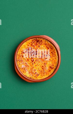 Creme brulee fatta in casa con crosta di caramello, in un vassoio di argilla, su sfondo verde senza cuciture. Torta alla crema pasticcera francese. Crema bruciata con zucchero di canna caramellato Foto Stock