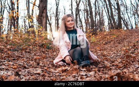 Una giovane donna piacevole in abiti casual con capelli lunghi è seduta nella foresta di autunno. Foto Stock