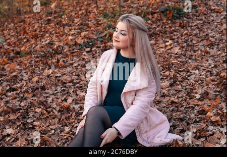 Una giovane donna piacevole in abiti casual con capelli lunghi è seduta nella foresta di autunno. Foto Stock
