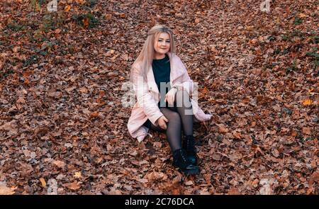 Una giovane donna piacevole in abiti casual con capelli lunghi è seduta nella foresta di autunno. Foto Stock