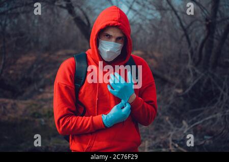 Giovane uomo in maschera medica indossando guanti in campagna. Uomo adulto che si protegge dalle malattie a piedi. Concetto di minaccia del coronavirus Foto Stock