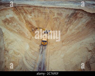 Escavatore e dumper. Vista aerea del carico di sabbia in un carrello. Un macchinario pesante - escavatore e camion stanno lavorando nella cava di sabbia. Foto Stock