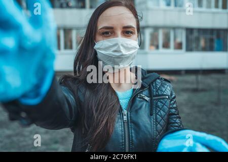 Ritratto di giovane donna in maschera medica sul viso in piedi per strada. La donna adulta ha coperto il suo viso con una maschera per proteggersi dalle malattie. Foto Stock