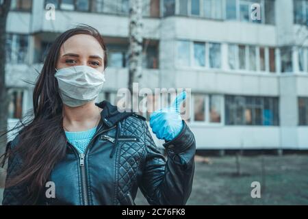 Ritratto di giovane donna in maschera medica sul viso in piedi per strada. La donna adulta ha coperto il suo viso con una maschera per proteggersi dalle malattie. Foto Stock