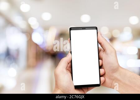 Uomo`s mano che tiene il cellulare smartphone con schermo vuoto a sfondo sfocato centro commerciale. Foto Stock