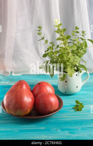 Pomodori rosa di paese di zucchero maturo su un tavolo di legno blu. Nella tazza - un mazzo di Melissa Foto Stock