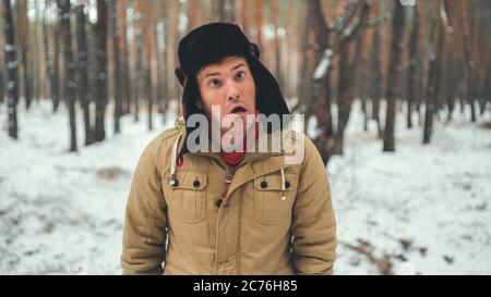Uomo grimaces in foresta nella stagione invernale. Ritratto di pazzo maschio che indossa copricapo e grimacing faccia da vicino nella foresta invernale. Foto Stock