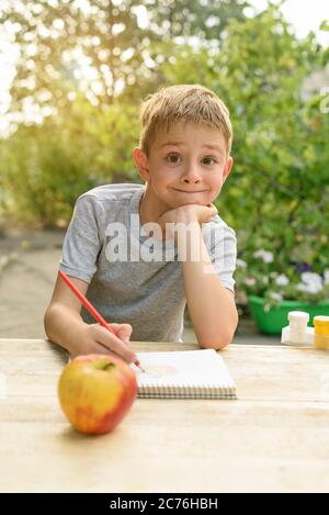 Il ragazzo carino disegna con matite ancora vita. Aria aperta. Giardino sullo sfondo. Concetto creativo. Foto Stock