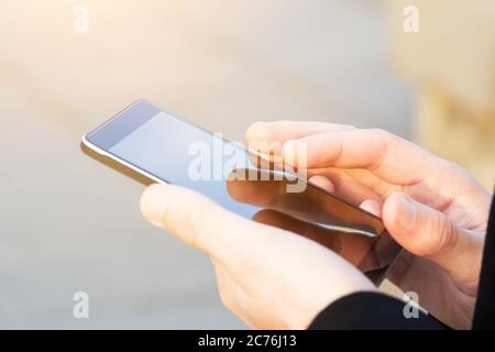 Uomo che usa il suo cellulare all'aperto, primo piano. Uomo che tiene lo smartphone con sfondo sfocato Foto Stock