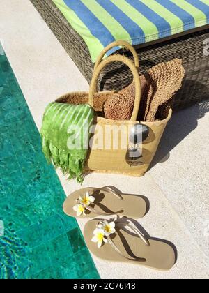 Flip-flop e un cesto con accessori estivi presso una piscina Foto Stock