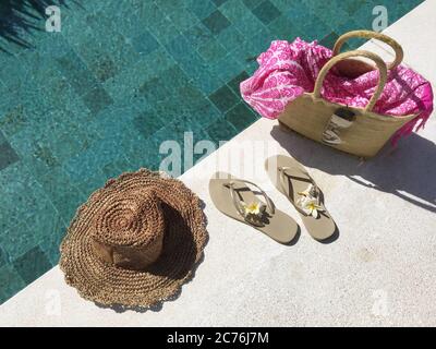 Flip-flop e un cesto con accessori estivi presso una piscina Foto Stock