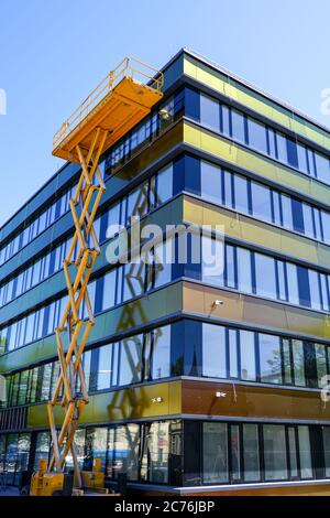 edificio moderno, con una facciata riparata con un ascensore a forbice giallo con una piattaforma Foto Stock