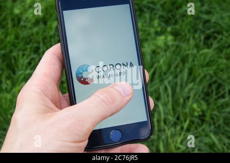Corona avvisa l'app del governo federale tedesco su uno smartphone tenuto in una mano dell'uomo. Foto Stock