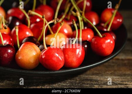 Ciliegie dolci su un piatto su una superficie di legno. Tasto basso. Foto Stock