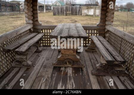 Tavolo in legno con panchine nel parco divertimenti. Terrazza recintata con tavolo e panchine in un parco vuoto durante la cupa giornata autunnale Foto Stock