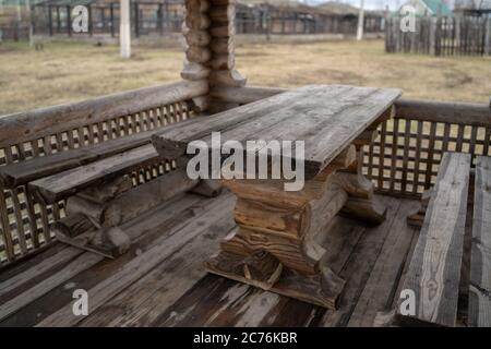 Tavolo in legno con panchine nel parco divertimenti. Terrazza recintata con tavolo e panchine in un parco vuoto durante la cupa giornata autunnale Foto Stock