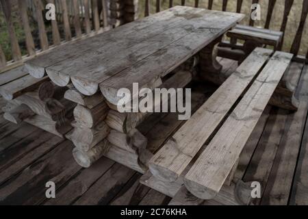 Tavolo in legno con panchine nel parco divertimenti. Terrazza recintata con tavolo e panchine in un parco vuoto durante la cupa giornata autunnale Foto Stock