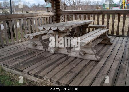 Tavolo in legno con panchine nel parco divertimenti. Terrazza recintata con tavolo e panchine in un parco vuoto durante la cupa giornata autunnale Foto Stock