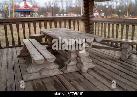 Tavolo in legno con panchine nel parco divertimenti. Terrazza recintata con tavolo e panchine in un parco vuoto durante la cupa giornata autunnale Foto Stock