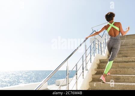 Bella donna dal retro in moderno vestito grigio da sport alzarsi da scale con bella vista mare Foto Stock