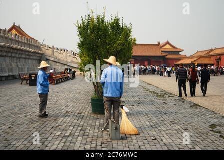 Due addetti alla manutenzione che hanno una conversazione nella zona della Città Proibita, indossando cappelli di paglia e magliette blu, turisti in background. Foto Stock