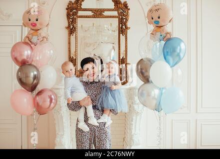 Ritratto di una donna sorridente che tiene i suoi nipoti gemelli il loro 1 ° compleanno Foto Stock