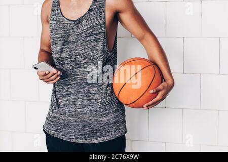 primo piano di un giovane irriconoscibile che guarda il suo smartphone mentre tiene un basket Foto Stock