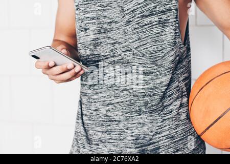 primo piano di un giovane irriconoscibile che guarda il suo smartphone mentre tiene un basket Foto Stock