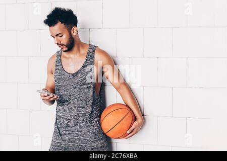 giovane uomo che guarda il suo smartphone mentre tiene un basket Foto Stock