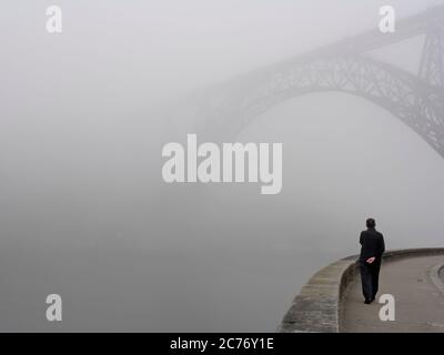 Porto, Portogallo - 25 aprile 2006: Uomo che cammina da solo sulla riva del fiume Douro vedendo uno dei famosi e bei ponti di Porto al mattino f Foto Stock