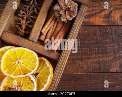 Composizione per le vacanze di Natale : bel primo piano di arance secche, bastoncini di cannella e stella Anis, coni di abete in una scatola di legno sullo sfondo di legno Foto Stock