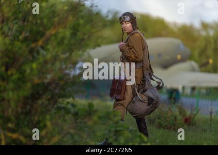 Una giovane pilota femminile in uniforme di piloti dell'esercito sovietico durante la seconda guerra mondiale Maglia militare con spalline di un maggiore, paracadute, volo helme Foto Stock