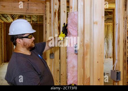 Lavoratore di costruzione che installa lo strato di isolamento termico sotto la parete usando lana minerale con fuoco morbido freddo della fibra di vetro Foto Stock