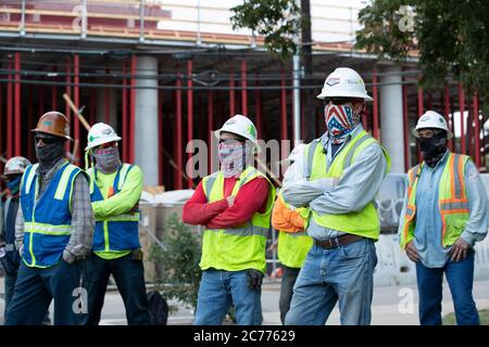 Austin, Texas USA 14 luglio 2020: I lavoratori del settore edile ascoltano le informazioni sulla sicurezza mentre si preparano per un turno di otto ore nel calore a 105 gradi del Texas. Gli equipaggi sono al secondo piano di un edificio a 53 piani, mentre prendono precauzioni contro la pandemia del coronavirus. Foto Stock