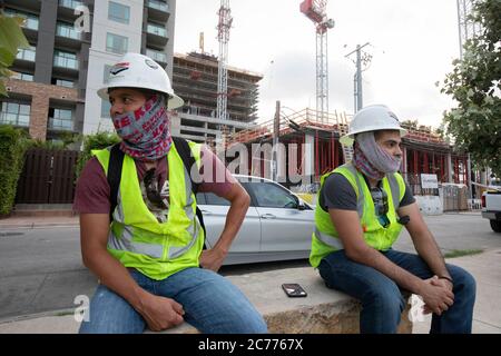 Austin, Texas USA 14 luglio 2020: I lavoratori del settore edile ascoltano le informazioni sulla sicurezza mentre si preparano per un turno di otto ore nel calore a 105 gradi del Texas. Gli equipaggi sono al secondo piano di un edificio a 53 piani, mentre prendono precauzioni contro la pandemia del coronavirus. Foto Stock